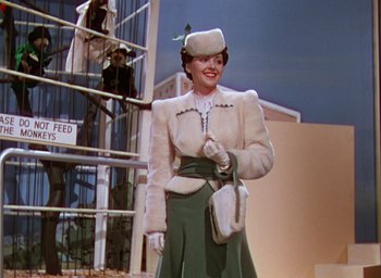 Movie still from “The Women” (1939), directed by George Cukor – A woman in a white coat and green skirt holding a purse; Medium shot, Low angle