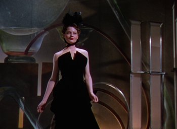 Movie still from “The Women” (1939), directed by George Cukor – A woman in a black dress is standing in front of a staircase; Medium shot, Low angle