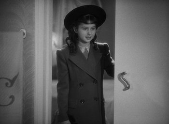 Movie still from “The Women” (1939), directed by George Cukor – A young girl in a suit and hat standing next to a door; Medium shot, High angle
