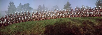 Movie still from “The Wonderful World of the Brothers Grimm” (1962), directed by Henry Levin – A large group of people dressed in military garb sitting on the grass; Extreme Wide shot, High angle