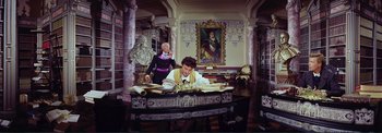 Movie still from “The Wonderful World of the Brothers Grimm” (1962), directed by Henry Levin – A man sitting at a desk in front of a painting; Wide shot, Low angle