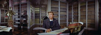 Movie still from “The Wonderful World of the Brothers Grimm” (1962), directed by Henry Levin – A man sitting at a table in a library; Medium shot, Low angle