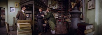 Movie still from “The Wonderful World of the Brothers Grimm” (1962), directed by Henry Levin – Two men standing next to each other in front of a bookcase; Wide shot, High angle