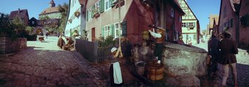 Movie still from “The Wonderful World of the Brothers Grimm” (1962), directed by Henry Levin – A woman and a man standing next to each other near barrels; Wide shot, High angle