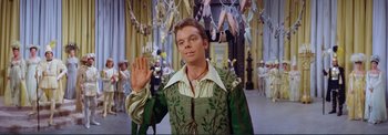 Movie still from “The Wonderful World of the Brothers Grimm” (1962), directed by Henry Levin – A man in a green and white costume holding a hand up; Medium shot, Low angle