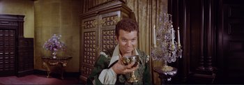 Movie still from “The Wonderful World of the Brothers Grimm” (1962), directed by Henry Levin – A young man holding a wine goblet in his hand; Medium shot, High angle