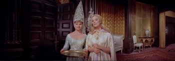 Movie still from “The Wonderful World of the Brothers Grimm” (1962), directed by Henry Levin – Two women dressed in costumes stand next to each other holding a tray; Medium shot, Low angle