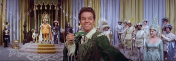 Movie still from “The Wonderful World of the Brothers Grimm” (1962), directed by Henry Levin – A man holding a green mask in front of a crowd; Close Up shot, High angle