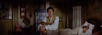 Movie still from “The Wonderful World of the Brothers Grimm” (1962), directed by Henry Levin – A man holding a dog while sitting on a chair; Medium shot, Low angle