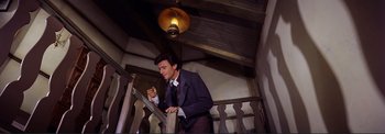 Movie still from “The Wonderful World of the Brothers Grimm” (1962), directed by Henry Levin – A man in a suit and tie standing next to a railing; Medium shot, High angle