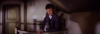 Movie still from “The Wonderful World of the Brothers Grimm” (1962), directed by Henry Levin – A man in a suit and tie leaning against a railing; Medium shot, High angle