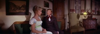 Movie still from “The Wonderful World of the Brothers Grimm” (1962), directed by Henry Levin – A man and a woman sitting next to each other in a room; Medium shot, Over the shoulder angle
