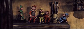Movie still from “The Wonderful World of the Brothers Grimm” (1962), directed by Henry Levin – A group of three figurines sitting on top of a table; Wide shot, Low angle