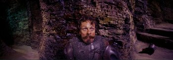 Movie still from “The Wonderful World of the Brothers Grimm” (1962), directed by Henry Levin – A man in a chain mail armor sitting in front of a brick wall; Medium shot, Overhead angle
