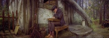 Movie still from “The Wonderful World of the Brothers Grimm” (1962), directed by Henry Levin – A man sitting on top of a wooden bench writing; Wide shot, High angle
