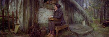 Movie still from “The Wonderful World of the Brothers Grimm” (1962), directed by Henry Levin – A man sitting on top of a wooden bench next to a building; Wide shot, High angle
