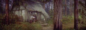 Movie still from “The Wonderful World of the Brothers Grimm” (1962), directed by Henry Levin – A man sitting on a bench in front of a hut; Wide shot, High angle