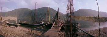 Movie still from “The Wonderful World of the Brothers Grimm” (1962), directed by Henry Levin – A man walking across a dock next to a body of water; Extreme Wide shot, High angle