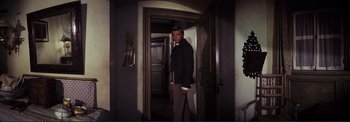 Movie still from “The Wonderful World of the Brothers Grimm” (1962), directed by Henry Levin – A man standing in a doorway wearing a suit and tie; Medium shot, Low angle