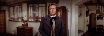 Movie still from “The Wonderful World of the Brothers Grimm” (1962), directed by Henry Levin – A man wearing a suit and tie standing in a room; Medium shot, Low angle