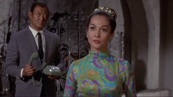 Movie still from “The Wrecking Crew” (1968), directed by Phil Karlson – A woman in a colorful dress standing in front of a man; Medium shot, Low angle