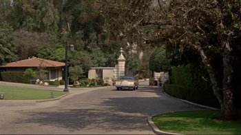 Movie still from “The Wrecking Crew” (1968), directed by Phil Karlson – A car driving down a street next to trees and bushes; Extreme Wide shot, High angle