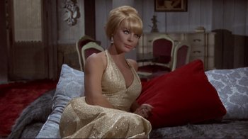 Movie still from “The Wrecking Crew” (1968), directed by Phil Karlson – A woman sitting on top of a bed in a gold dress; Medium shot, Low angle