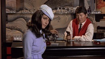 Movie still from “The Wrecking Crew” (1968), directed by Phil Karlson – A woman sitting at a bar with a man sitting at the bar; Medium shot, Low angle
