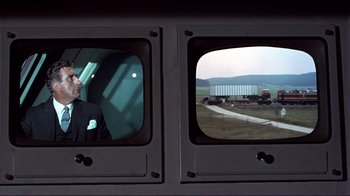 Movie still from “The Wrecking Crew” (1968), directed by Phil Karlson – A view from a train window of a truck and a man; Medium shot, Over the shoulder angle