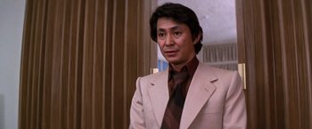 Movie still from “The Yakuza” (1974), directed by Sydney Pollack – A man wearing a suit and tie in front of a curtain; Close Up shot, Low angle