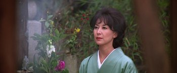 Movie still from “The Yakuza” (1974), directed by Sydney Pollack – A woman wearing a green robe standing next to flowers; Close Up shot, Low angle
