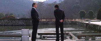 Movie still from “The Yakuza” (1974), directed by Sydney Pollack – Two men standing next to each other near a body of water; Wide shot, Over the shoulder angle