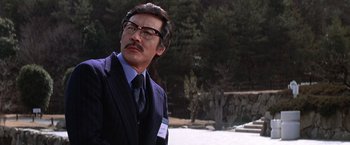 Movie still from “The Yakuza” (1974), directed by Sydney Pollack – A man in a suit and tie standing in front of trees; Close Up shot, Low angle