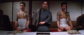 Movie still from “The Yakuza” (1974), directed by Sydney Pollack – A man standing next to two tattooed men; Medium shot, Low angle