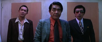 Movie still from “The Yakuza” (1974), directed by Sydney Pollack – A man in a suit and tie standing in front of a wall; Medium shot, Low angle