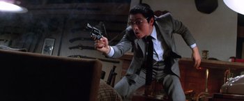 Movie still from “The Yakuza” (1974), directed by Sydney Pollack – A man in a suit and tie holding a gun in his hand; Medium shot, Low angle