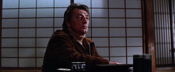 Movie still from “The Yakuza” (1974), directed by Sydney Pollack – A man sitting at a table in front of a cup; Medium shot, Low angle