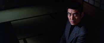 Movie still from “The Yakuza” (1974), directed by Sydney Pollack – A man wearing a suit and tie in a dark room; Close Up shot, Low angle