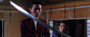 Movie still from “The Yakuza” (1974), directed by Sydney Pollack – A man in a red jacket holding two swords in front of another man in a blue suit; Medium shot, Low angle