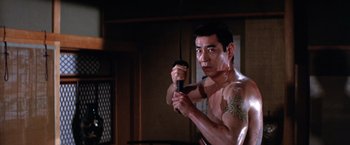 Movie still from “The Yakuza” (1974), directed by Sydney Pollack – A shirtless man holding a microphone in a room; Medium shot, Low angle