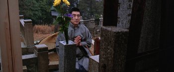 Movie still from “The Yakuza” (1974), directed by Sydney Pollack – A man kneeling down in front of a flower in a cemetery; Medium shot, Low angle