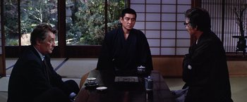 Movie still from “The Yakuza” (1974), directed by Sydney Pollack – A man sitting at a table with a cup of tea; Medium shot, Over the shoulder angle