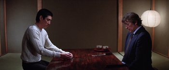 Movie still from “The Yakuza” (1974), directed by Sydney Pollack – A man sitting at a table with a knife and a pair of scissors; Medium shot, Over the shoulder angle