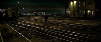 Movie still from “The Yards” (2000), directed by James Gray – A man standing on train tracks at a train station at night; Extreme Wide shot, High angle