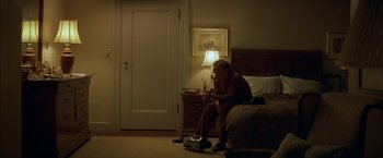 Movie still from “The Yards” (2000), directed by James Gray – An older man sitting on a bed next to a lamp; Wide shot, High angle