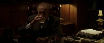 Movie still from “The Yards” (2000), directed by James Gray – An older man sitting at a table drinking a glass of whiskey; Medium shot, Low angle