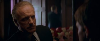 Movie still from “The Yards” (2000), directed by James Gray – A man in a suit and tie sitting in front of a bunch of flowers; Close Up shot, Over the shoulder angle