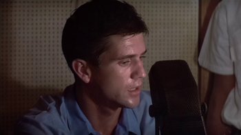 Movie still from “The Year of Living Dangerously” (1982), directed by Peter Weir – A man is sitting in front of a microphone; Close Up shot, Low angle