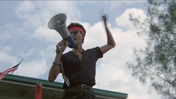 Movie still from “The Year of Living Dangerously” (1982), directed by Peter Weir – A person with a megaphone on a sunny day; Medium shot, Low angle