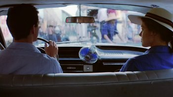 Movie still from “The Year of Living Dangerously” (1982), directed by Peter Weir – A man sitting in the back seat of a car; Medium shot, Over the shoulder angle